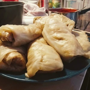 Mehrere Kohlrouladen liegen auf einem blauen Teller. Im Hintergrund ist ein kleiner Topf mit Tomatensauce zu erkennen.